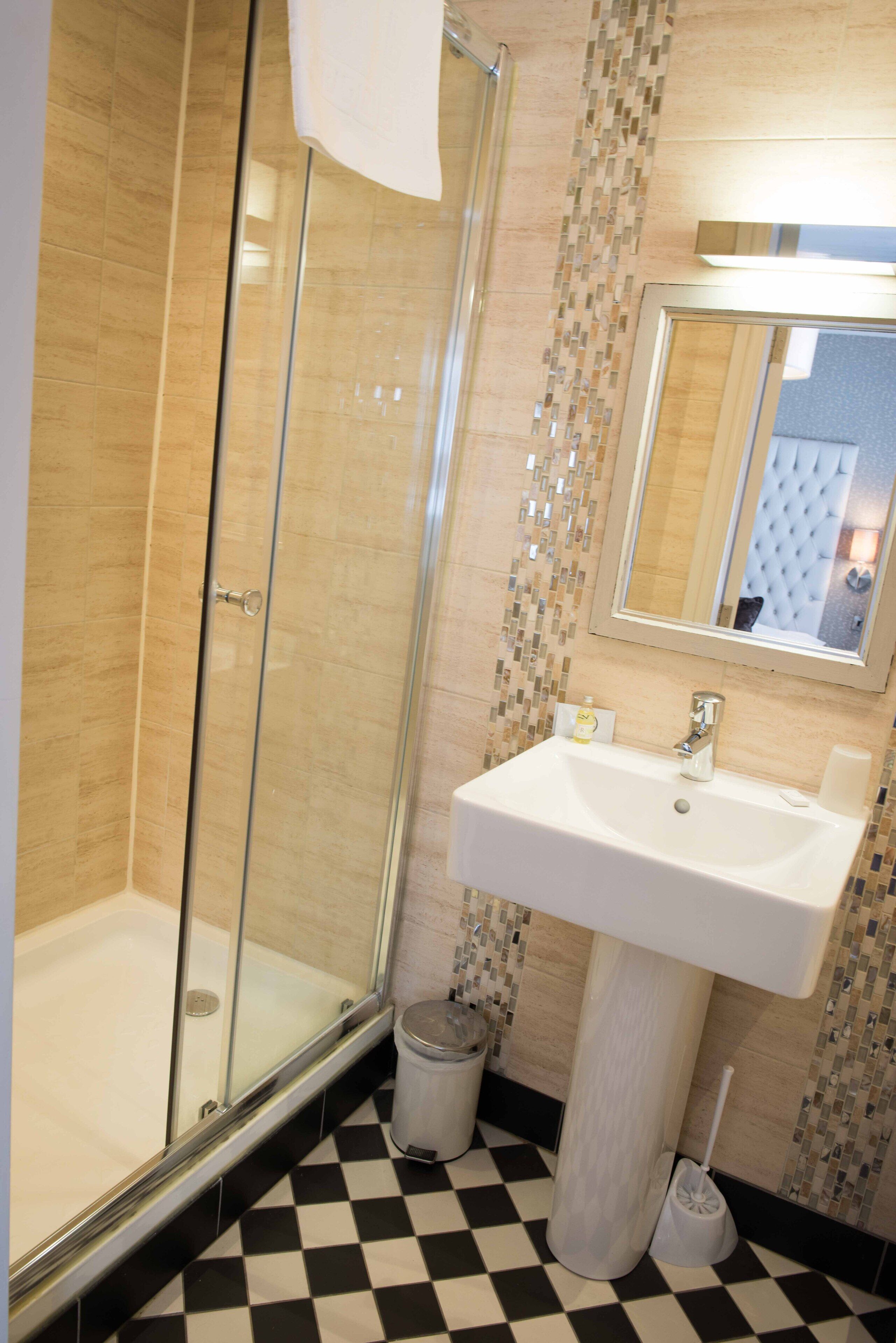 Un baño con cabina de ducha de vidrio, un lavabo blanco y piso de baldosas.