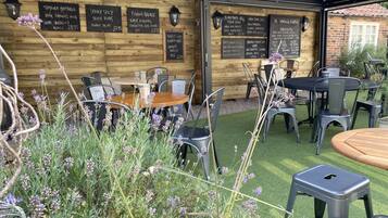 Un comedor al aire libre con paredes de madera y pizarras con menús que incluyen platos como 'Temura Battered King Prawns' y 'Sticky Spicy Belly Pork'.