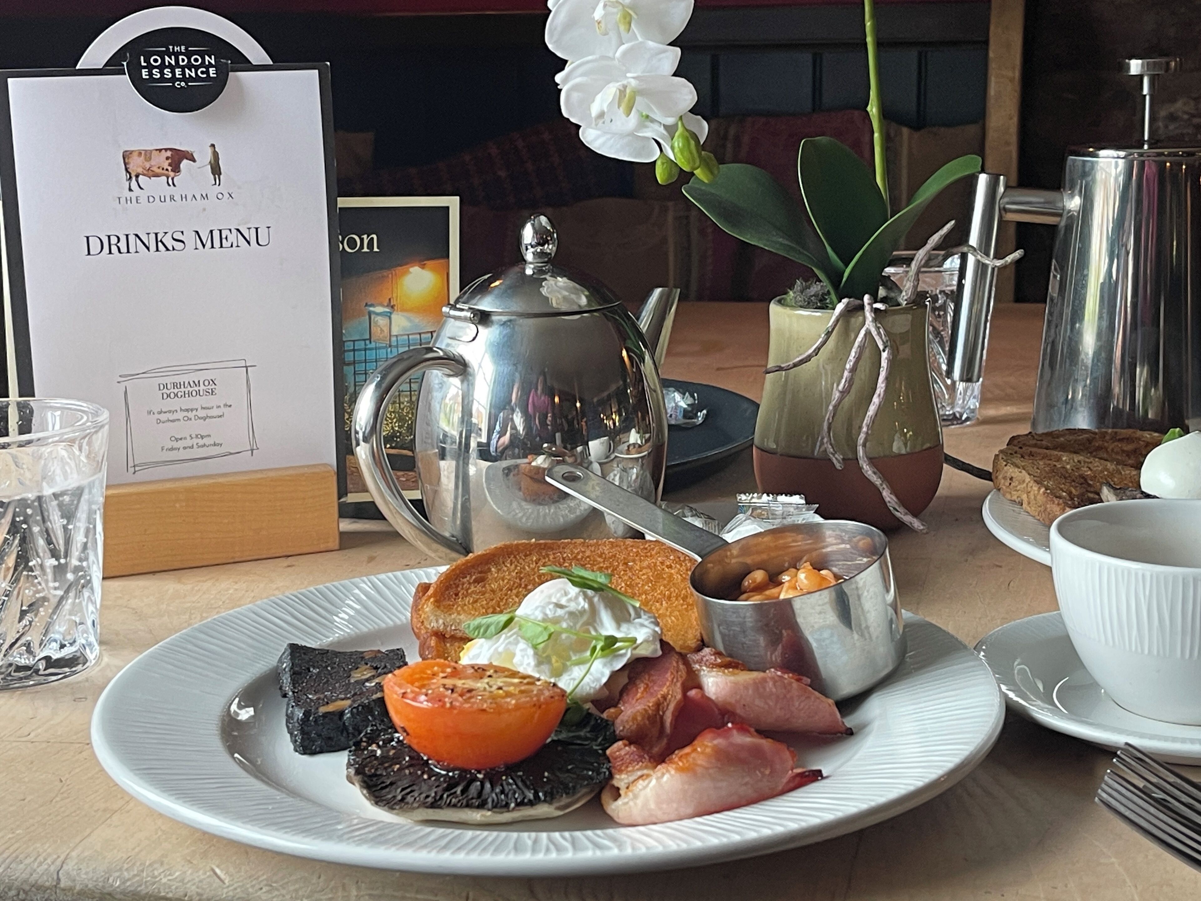 A breakfast setting with a plate of food, a teapot, a pitcher, and a menu.