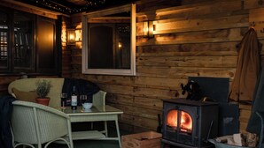 A cozy cabin interior with a wooden interior, a table with a bottle and glasses, a wicker chair, a fireplace, and a coat hanging on the wall. - The Durham Ox (York)