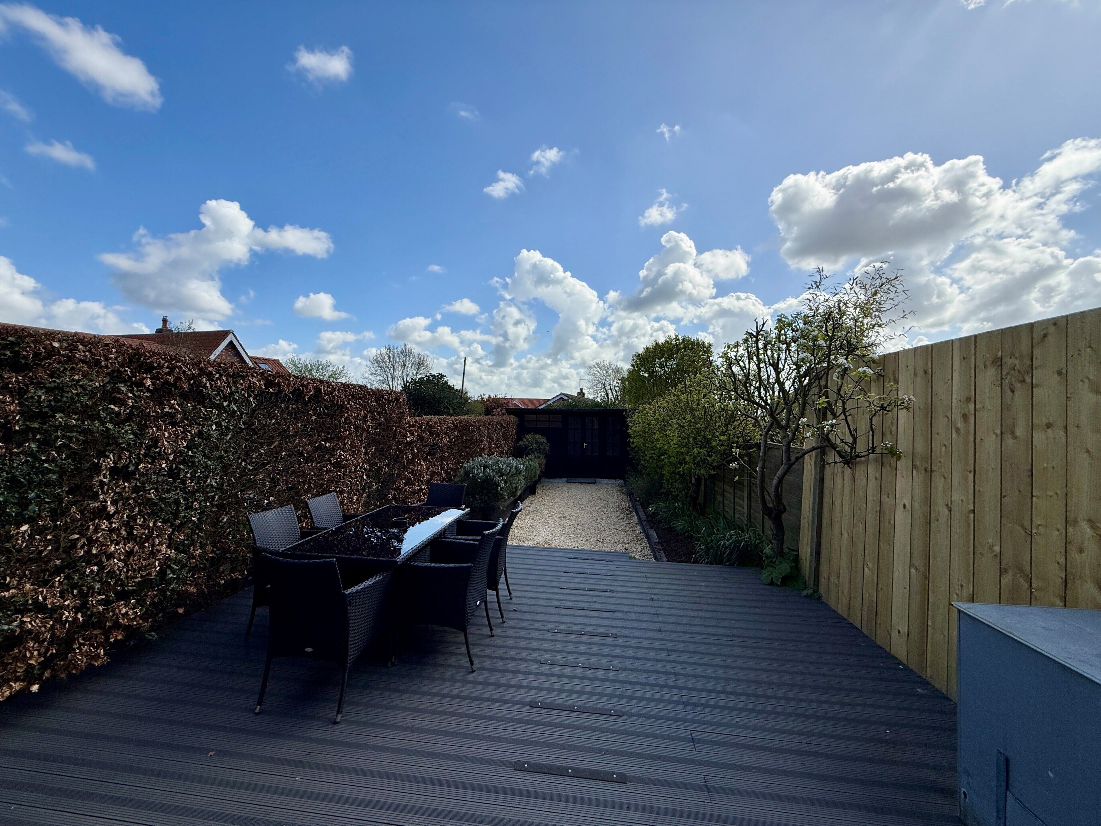 A wooden deck with outdoor furniture, a hedge, and a wooden fence.