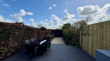 A wooden deck with outdoor furniture, a hedge, and a wooden fence.