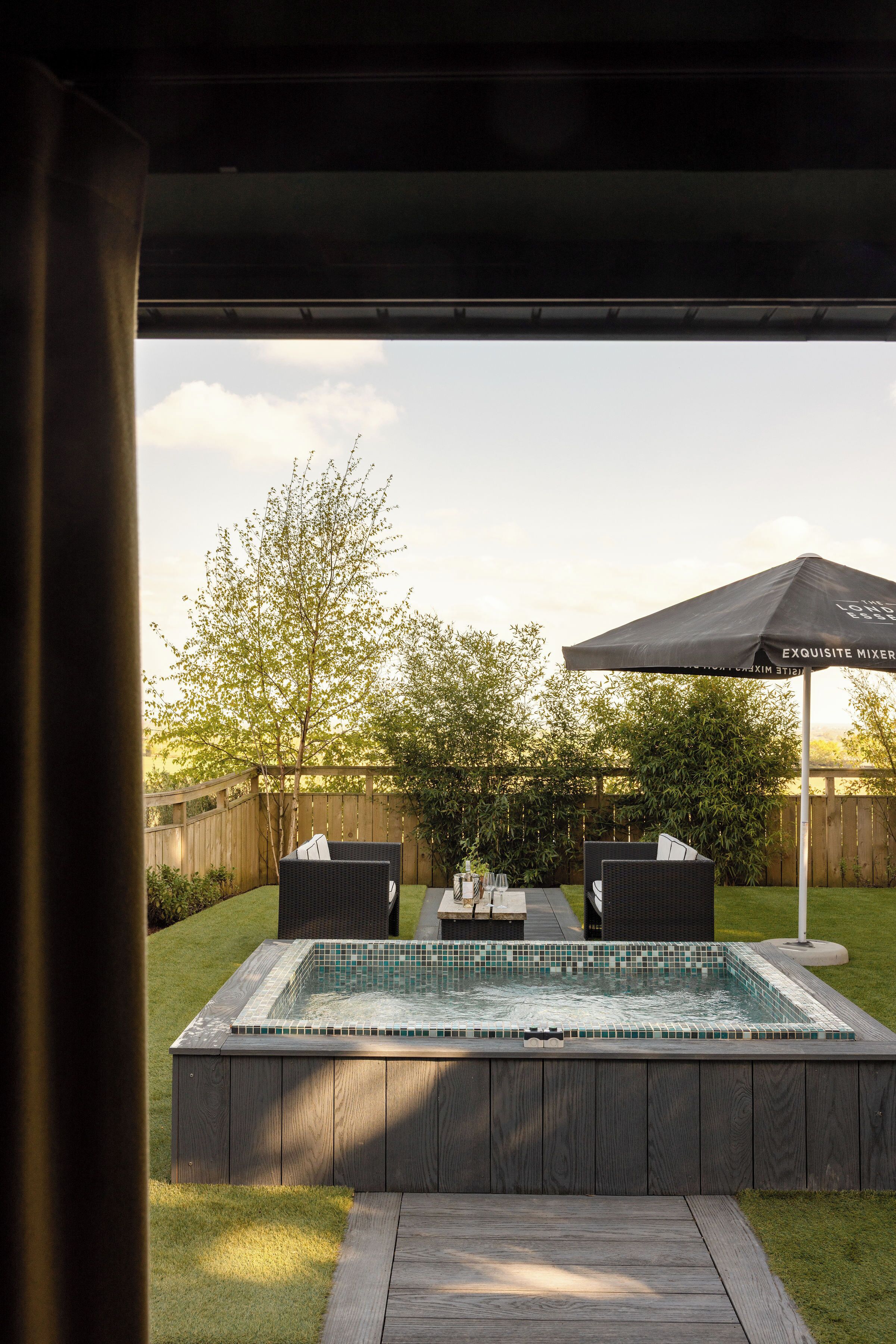 Ein Garten mit Whirlpool, zwei Korbstühlen und einem Tisch mit Sonnensegel.