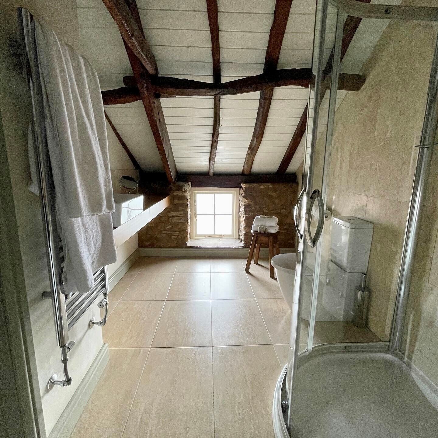 A bathroom with a stone wall, a window, a shower, and a towel hanging on a rack.