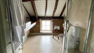 A bathroom with a stone wall, a window, a shower, and a towel hanging on a rack.
