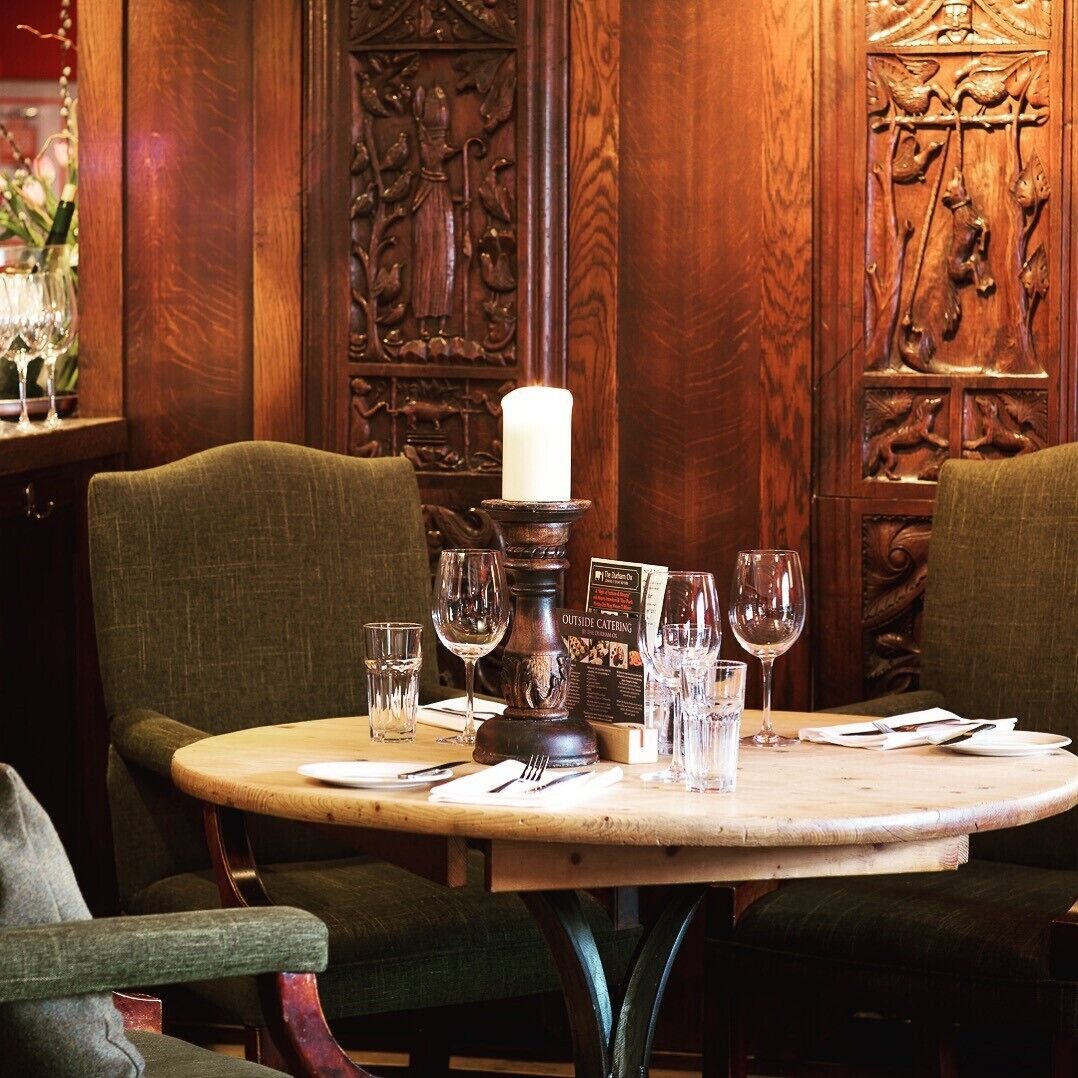 A dining table with a candle centerpiece, surrounded by chairs, in a room with ornate wooden paneling.