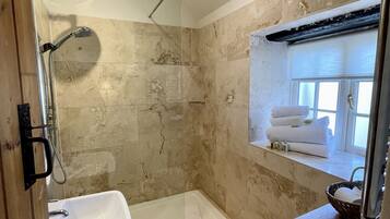 A bathroom with a glass-enclosed shower, a sink, and a window with towels.