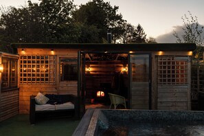 Une cabane en bois avec une porte en verre, une petite piscine et une cheminée.