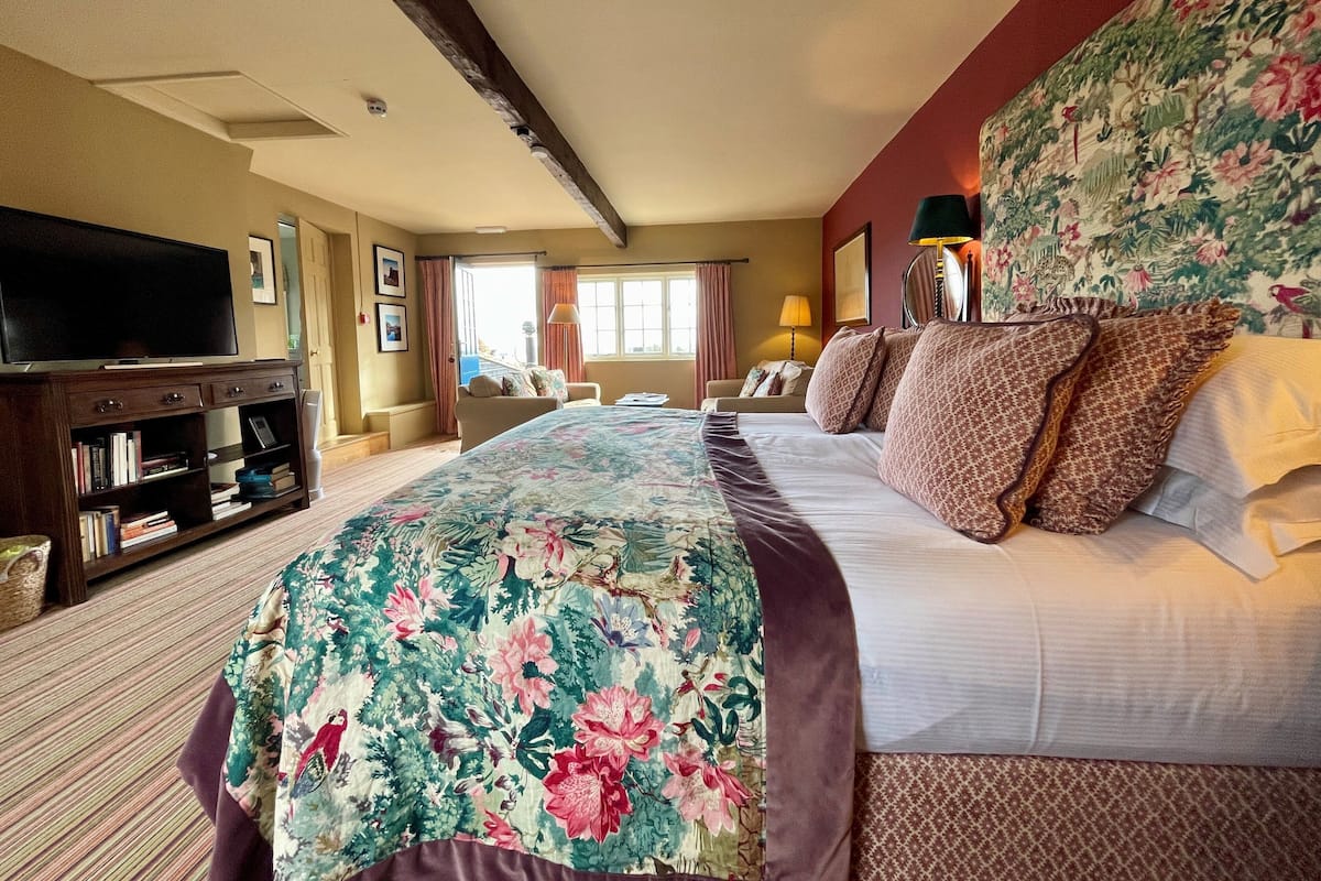 A hotel room with a large bed, a TV, a bookshelf, and a window with curtains.