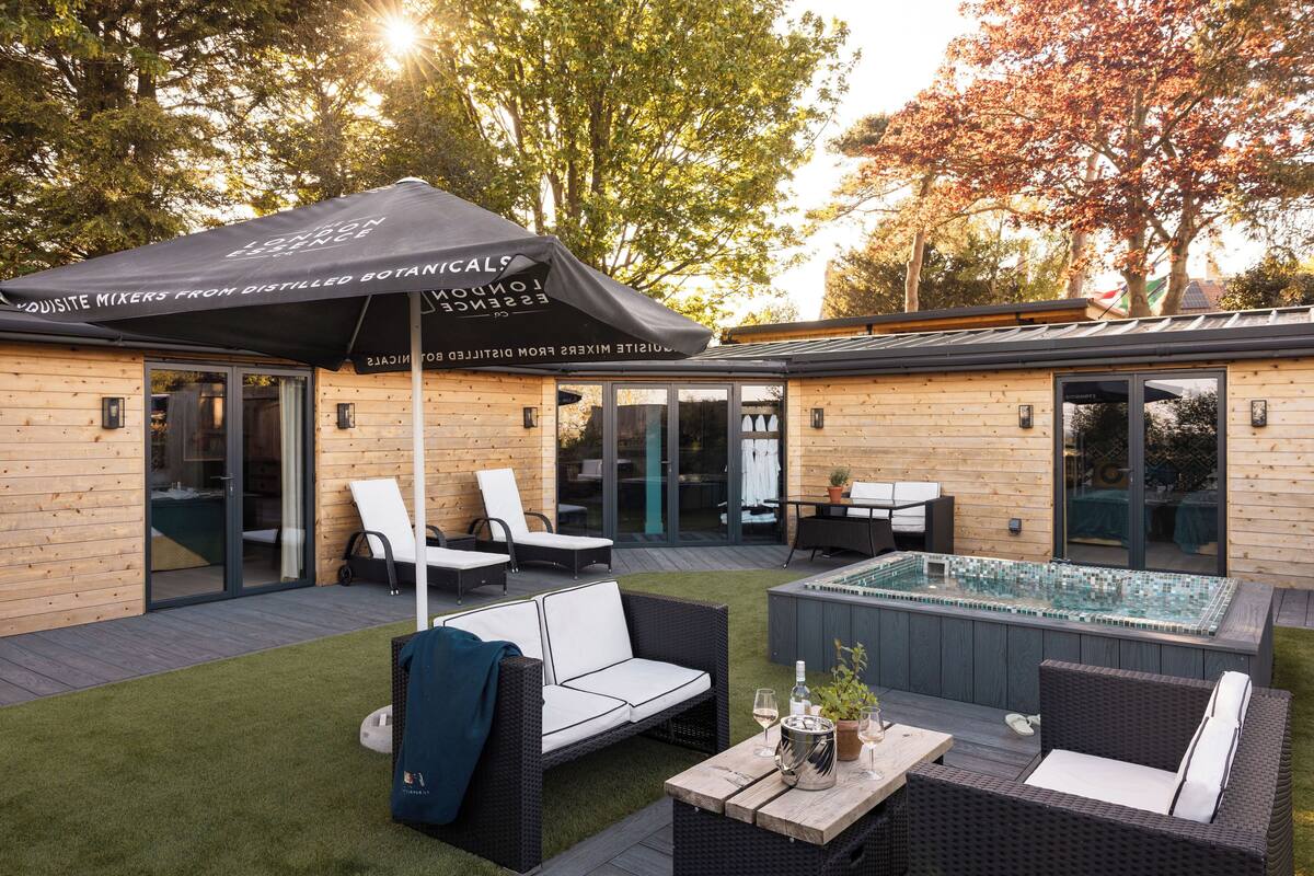 A wooden building with a patio area featuring outdoor furniture, a hot tub, and a covered umbrella.