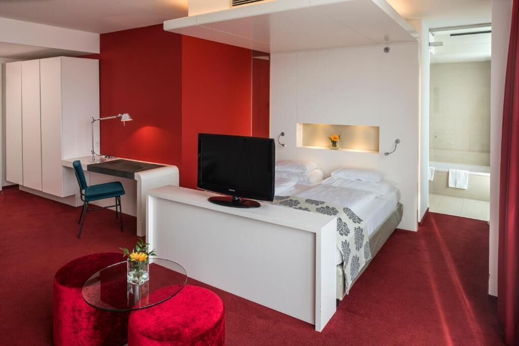 Una habitación de hotel moderna con cama, escritorio, televisor y una pequeña zona de estar.