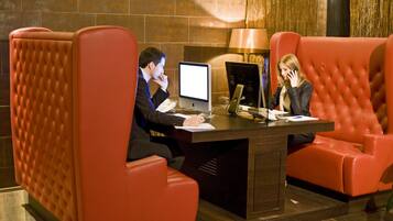 Een moderne hotellobby met een receptiebalie, twee rode leren fauteuils en een groot raam met uitzicht op de stad.