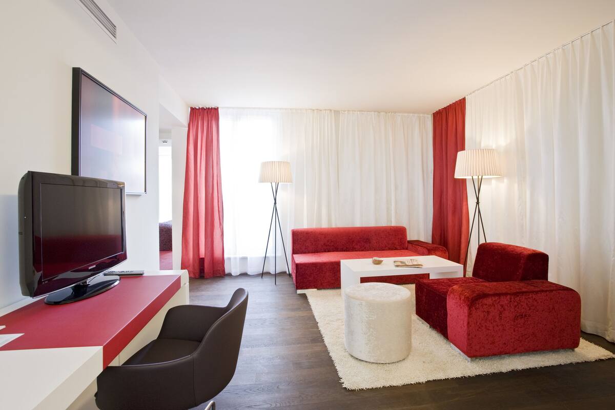 Un salon moderne avec un téléviseur à écran plat, des canapés rouges, une table basse blanche et deux lampadaires.