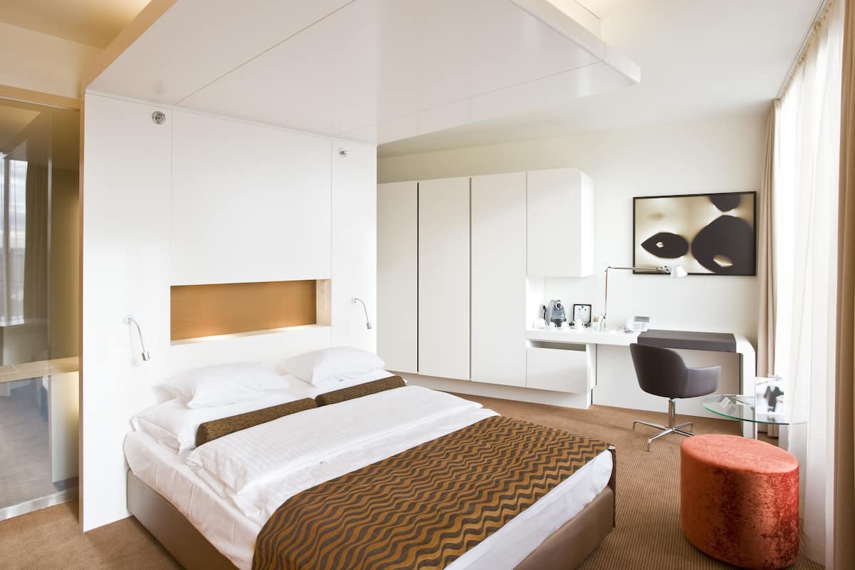 Une chambre d’hôtel moderne équipée d’un grand lit, d’un bureau, d’une chaise et d’une cloison en verre.