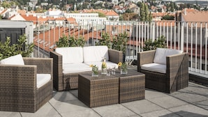 Terraza en la azotea con mobiliario de mimbre, una mesa de vidrio y vistas a un paisaje urbano.