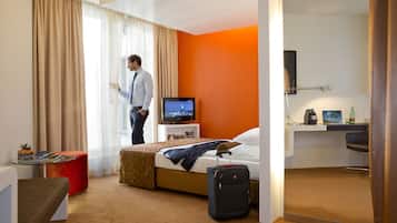 A hotel room with a bed, a desk, a television, a suitcase, and a window with curtains.