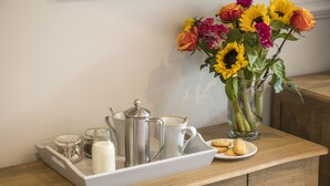 Une table en bois sur laquelle se trouve un plateau avec une théière, des tasses et une assiette de biscuits. Un vase contenant des tournesols et des roses est également posé sur la table.