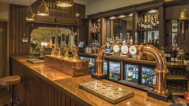 Un espace bar avec des robinets à bière en cuivre, une caisse enregistreuse et des étagères remplies de bouteilles.