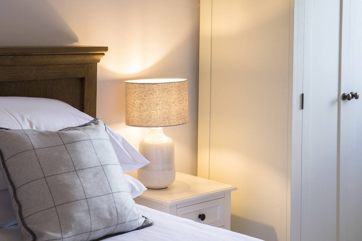 Cama bem arrumada com travesseiro e abajur sobre a mesa de cabeceira.