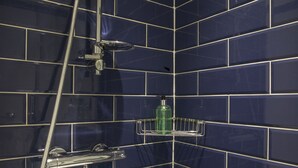 Une salle de bain avec des carreaux bleu foncé, une pomme de douche chromée et un distributeur de savon posé sur une étagère.