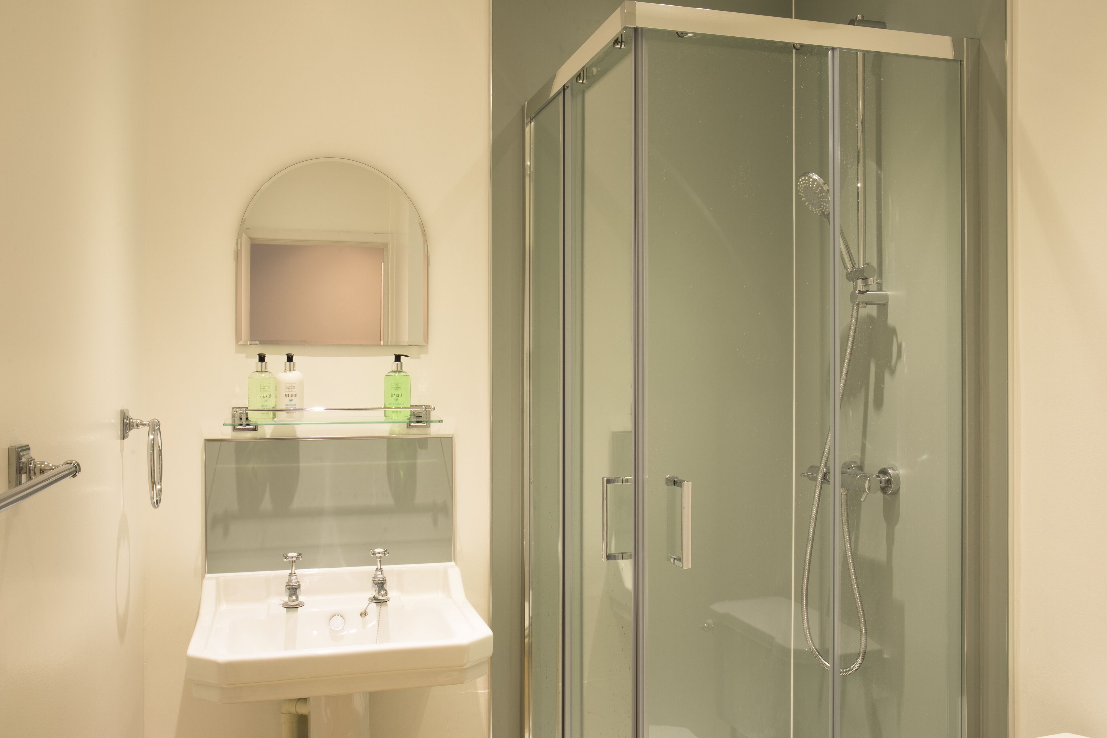A bathroom with a glass-enclosed shower, a sink, and a mirror above it.