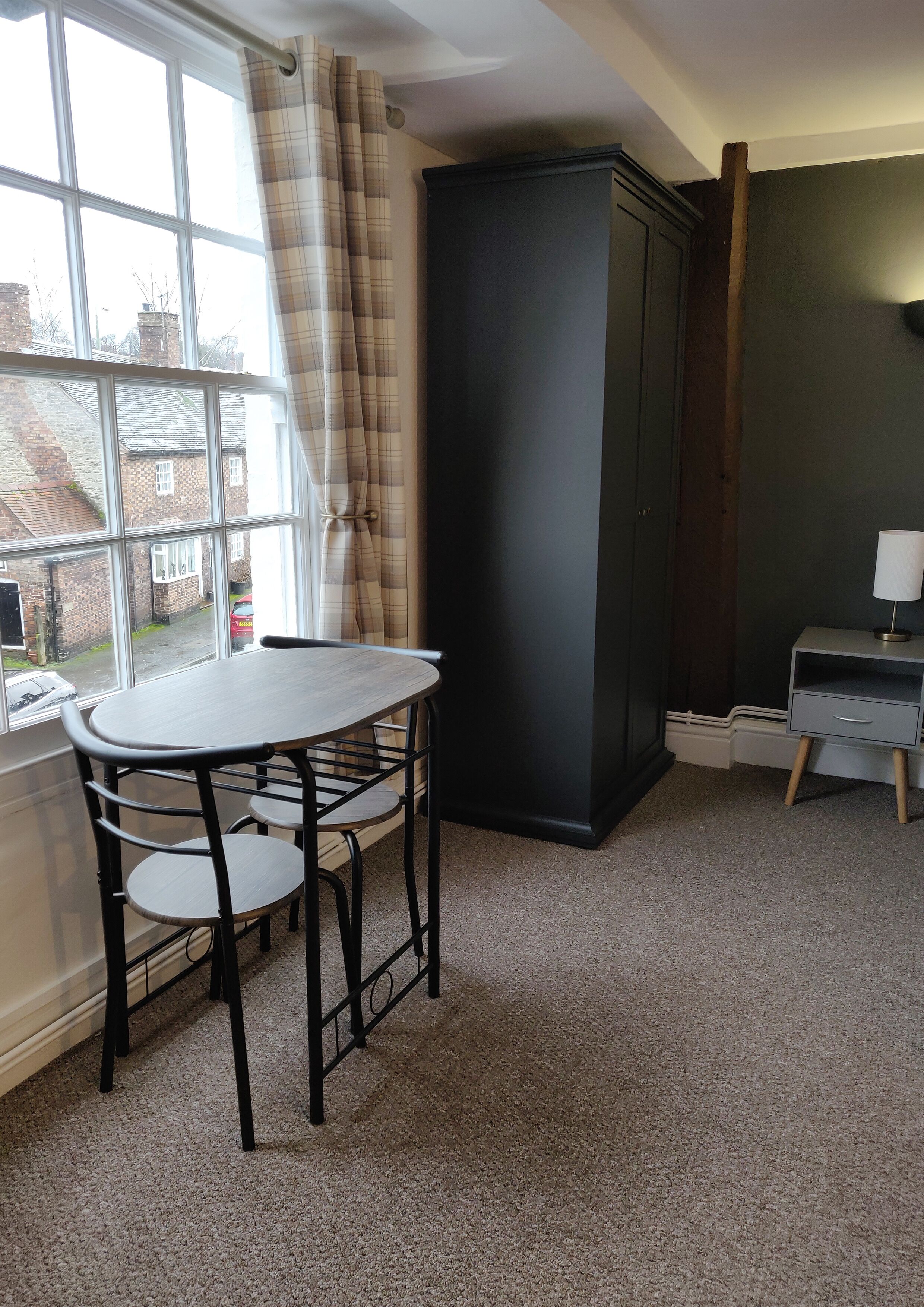A room with a window, a table with chairs, a cabinet, and a desk with a lamp.