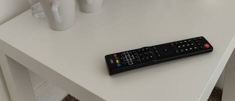 A white desk with a black coffee maker, three white mugs, a remote control, and a bowl containing various items.