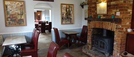 A cozy restaurant interior with brick fireplace, wooden tables, and red leather booths.