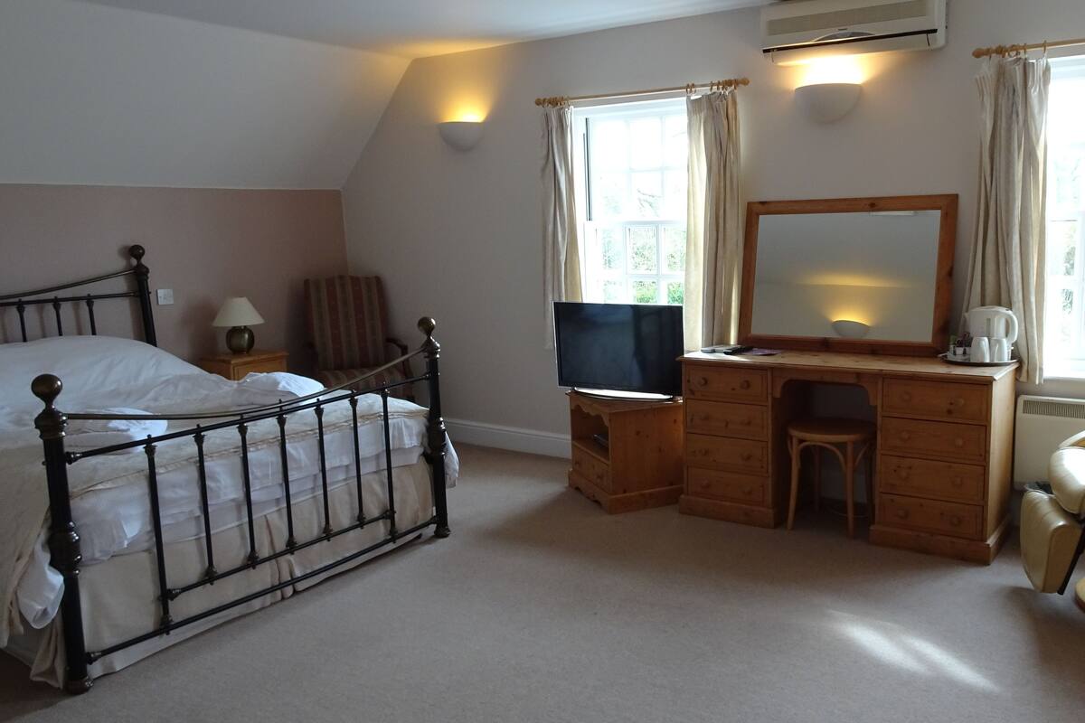 A bedroom with a bed, a wooden desk with a mirror, a television, and a chair.