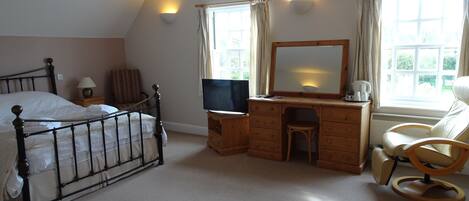 A bedroom with a bed, a wooden desk with a mirror, a television, and a chair.