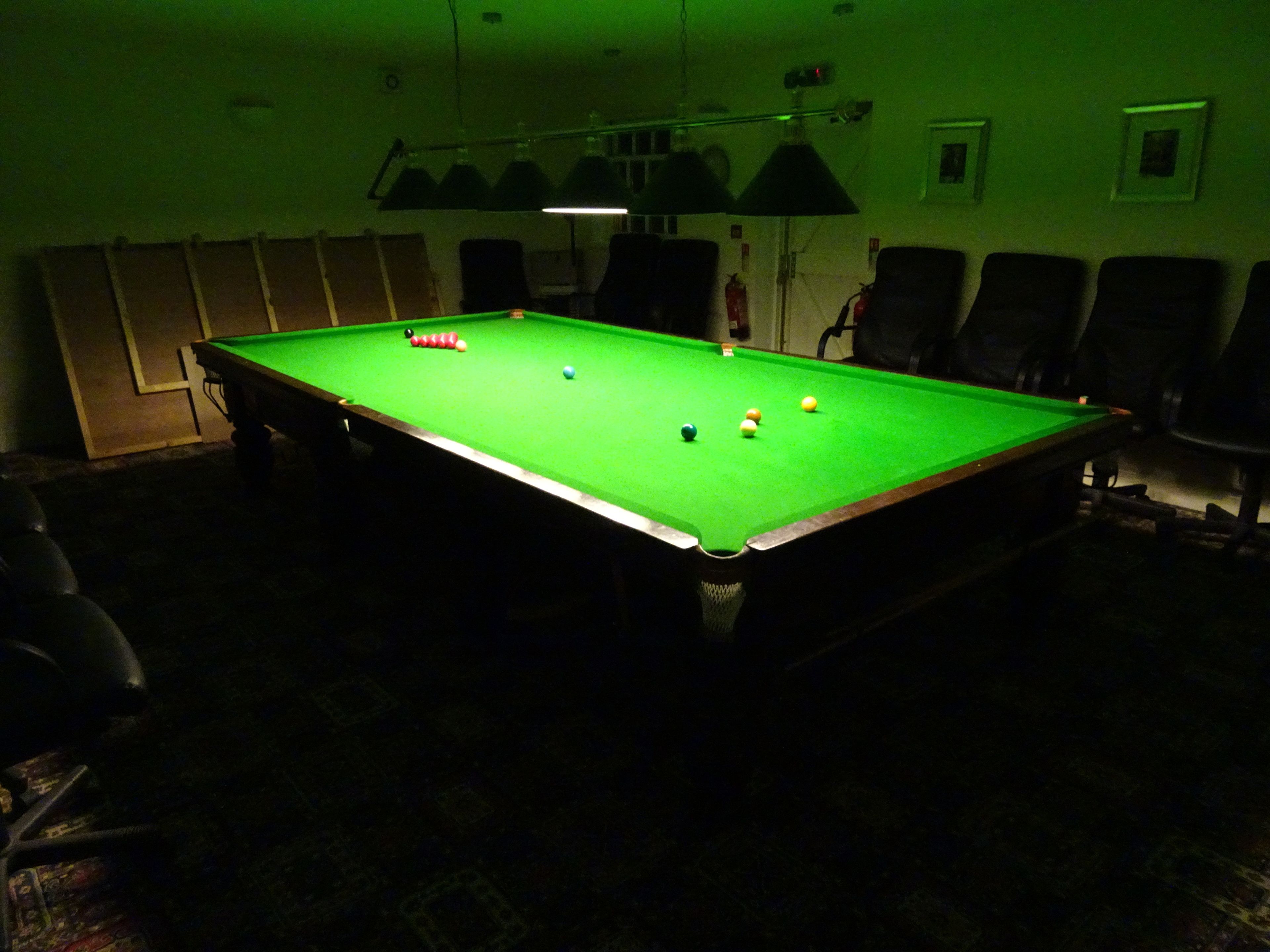 A pool table in a dimly lit room with chairs around it.