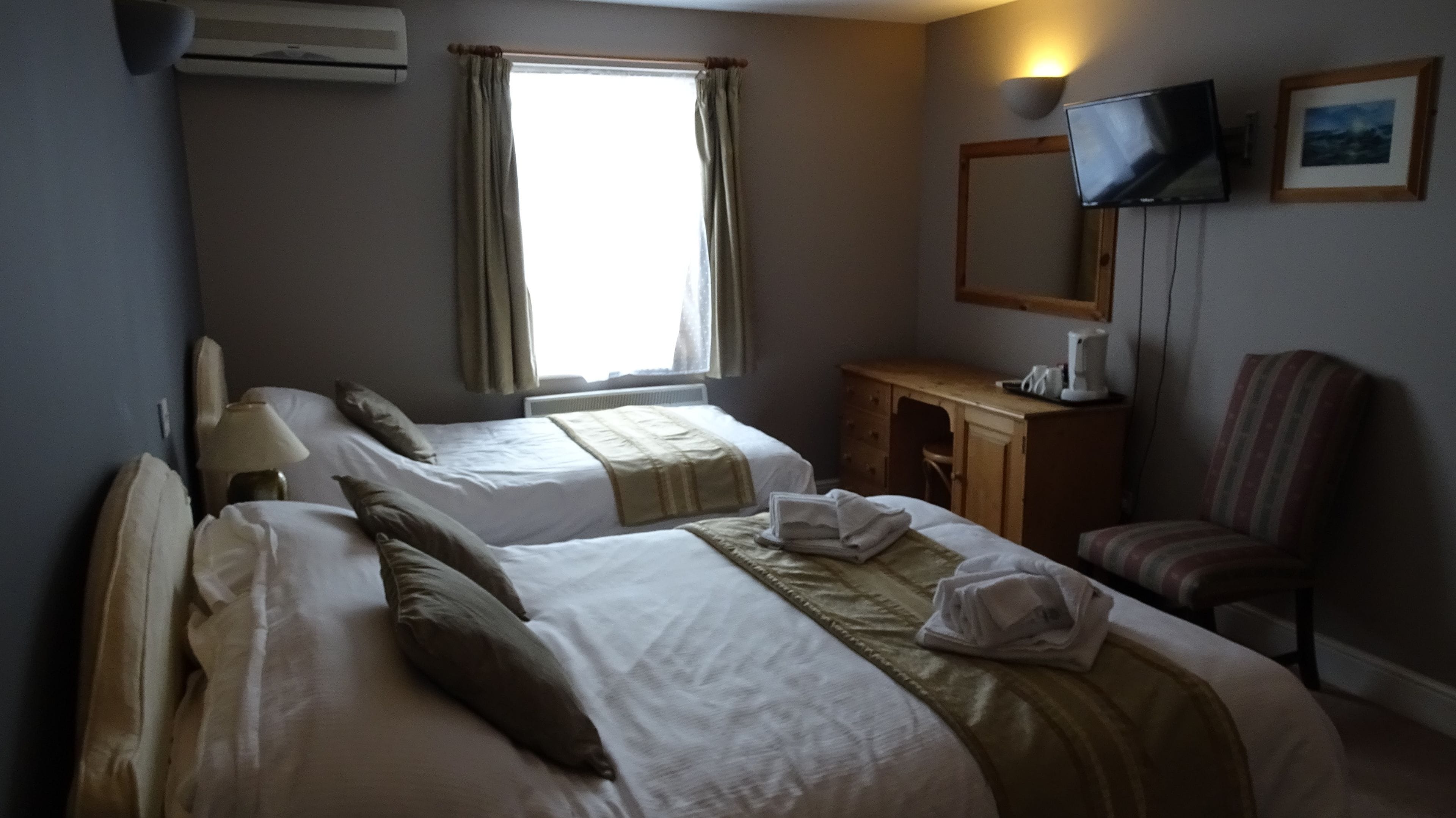 A hotel room with two beds, a desk, a chair, a television, and a window with curtains.