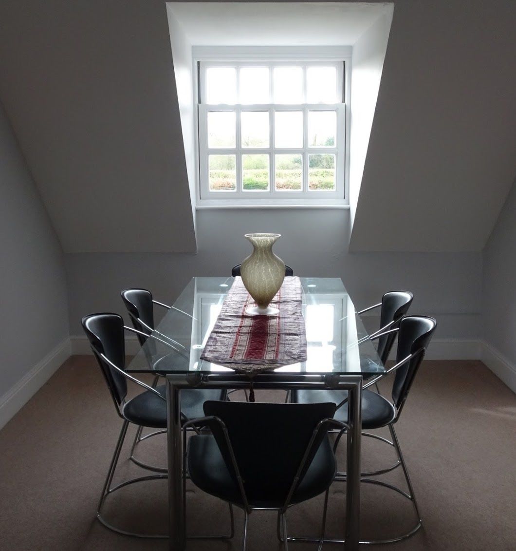 A dining table with a glass top and six black chairs, a vase on the table, and a window above.
