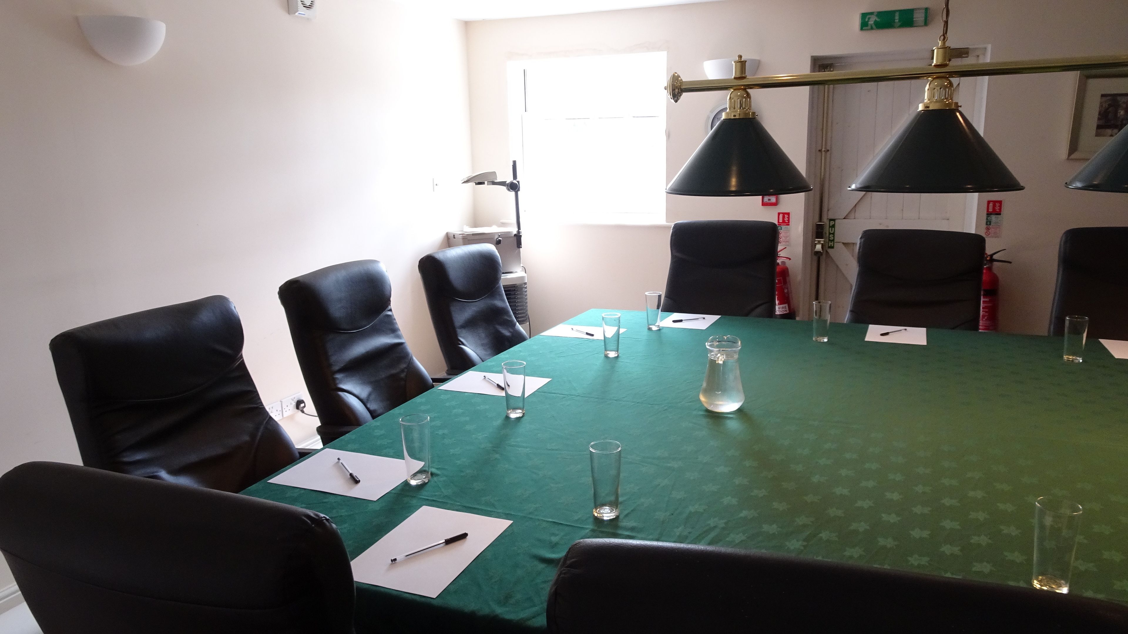 Une salle de conférence avec une table verte, des chaises noires et des lampes suspendues au plafond.