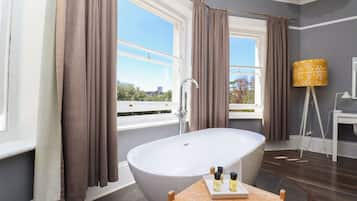 A modern bathroom with a freestanding bathtub, large windows with curtains, and a wooden table with toiletries.