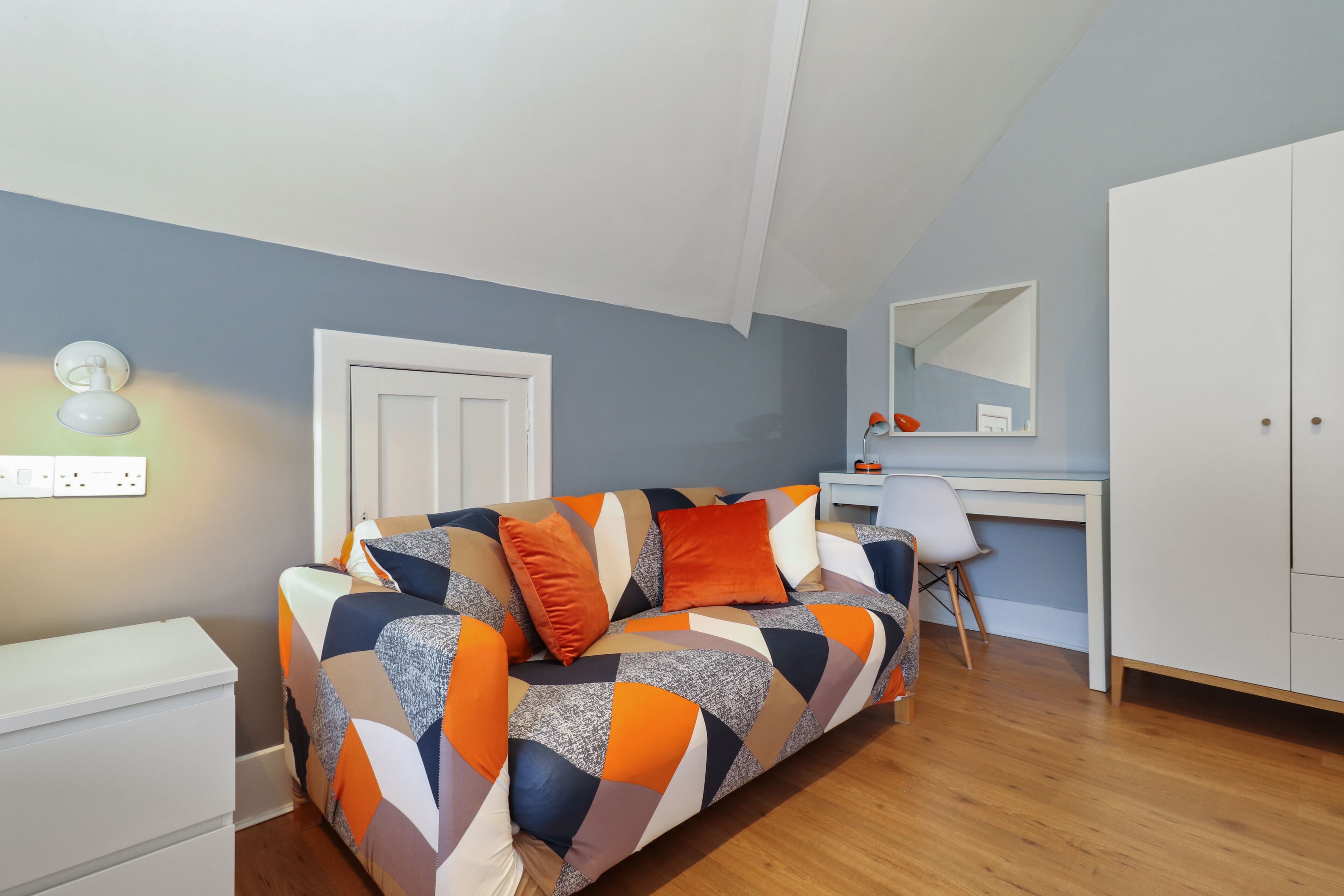 Une chambre moderne avec un canapé aux motifs géométriques, un bureau blanc et une armoire.