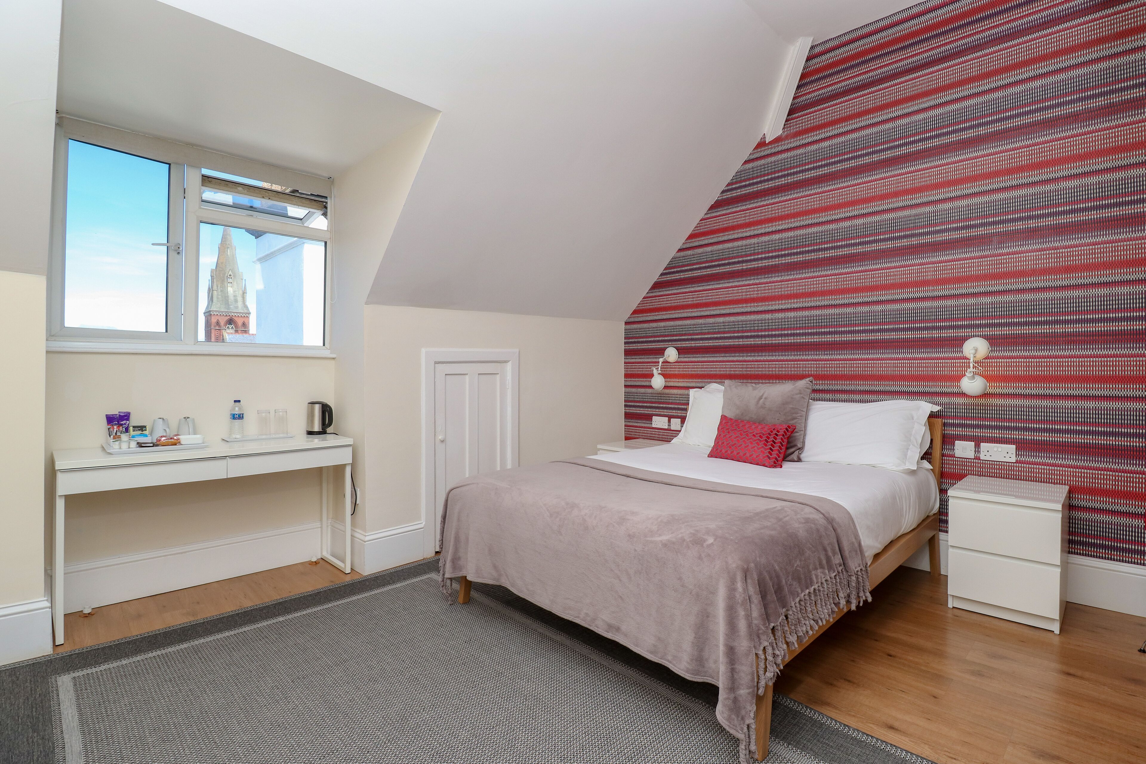 A bedroom with a bed, bedside tables, a desk, a window, and a patterned wall.