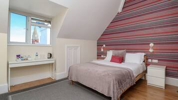 A bedroom with a bed, bedside tables, a desk, a window, and a patterned wall.
