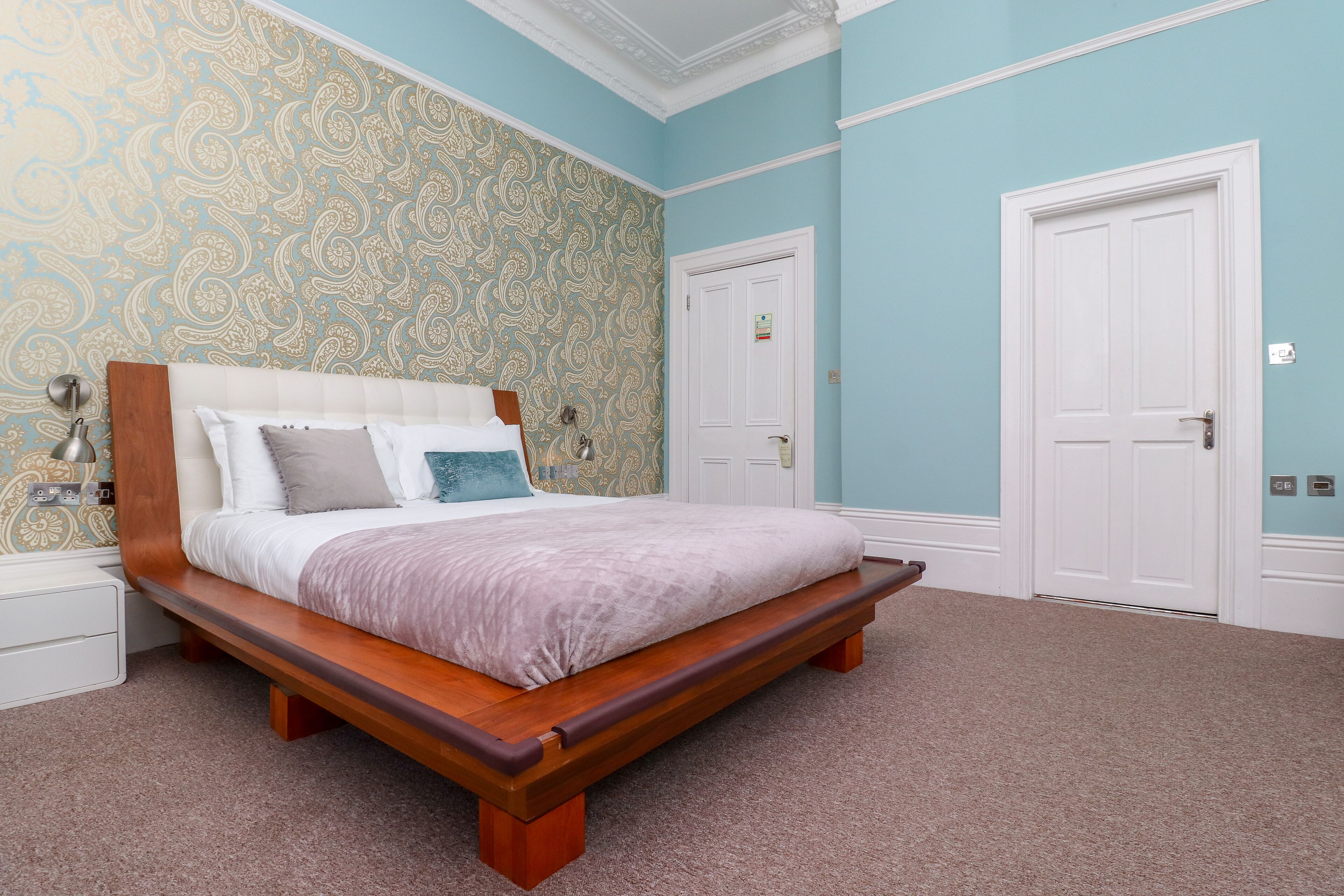 A bedroom with a bed, a nightstand, a wall with a patterned wallpaper, and two doors.