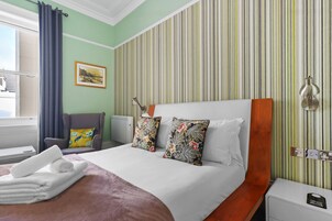 A hotel room with a bed, a chair, a table, and a window.