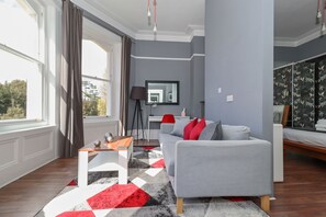 A modern living room with a grey sofa, a wooden coffee table, and a red and black patterned rug. - Ravilious (Eastbourne)