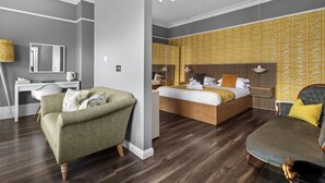 Una habitación de hotel moderna con una cama grande, una zona de estar con sofá y sillón, un escritorio y un espejo.