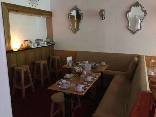 Un coin repas avec une table en bois dressée pour quatre personnes, un canapé et deux tabourets de bar.