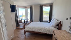 A bedroom with a wooden bed, a wooden dresser, a TV, and a view of the outdoors. - The Harbour Lights (Ilfracombe)