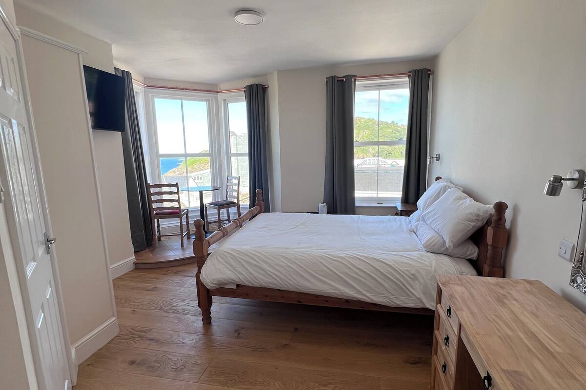 A bedroom with a wooden bed, a wooden dresser, a TV, and a view of the outdoors.