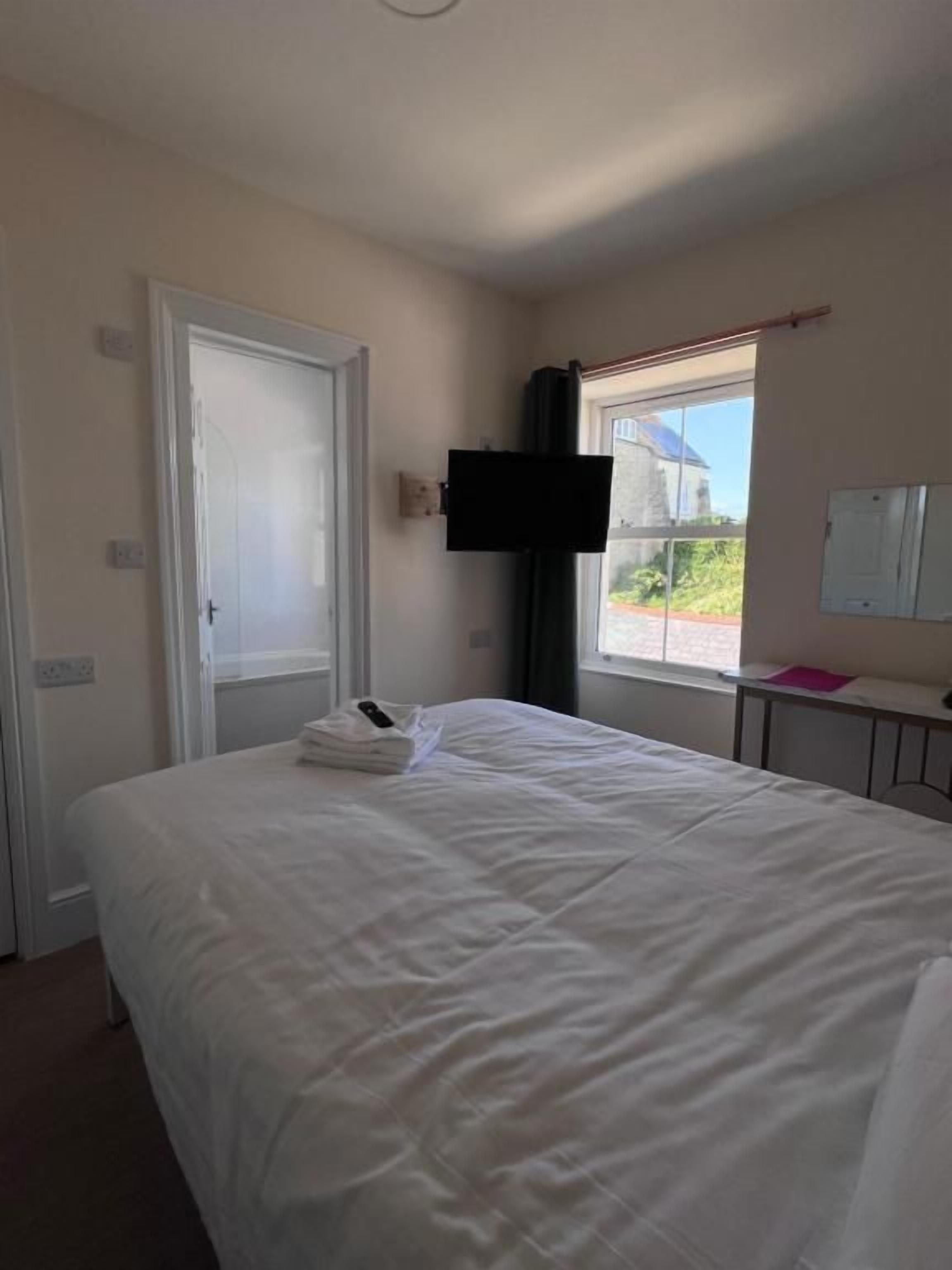 A hotel room with a bed, a television mounted on the wall, a window, and a door.