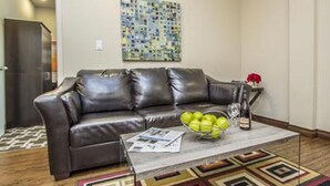A living room with a brown leather sofa, a coffee table with a bowl of apples, and a patterned rug. - The Harbour Lights (Ilfracombe)