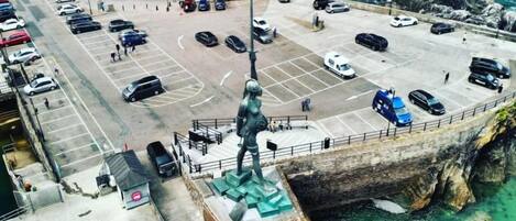 Un parking avec des véhicules, une statue et une vue sur la côte.