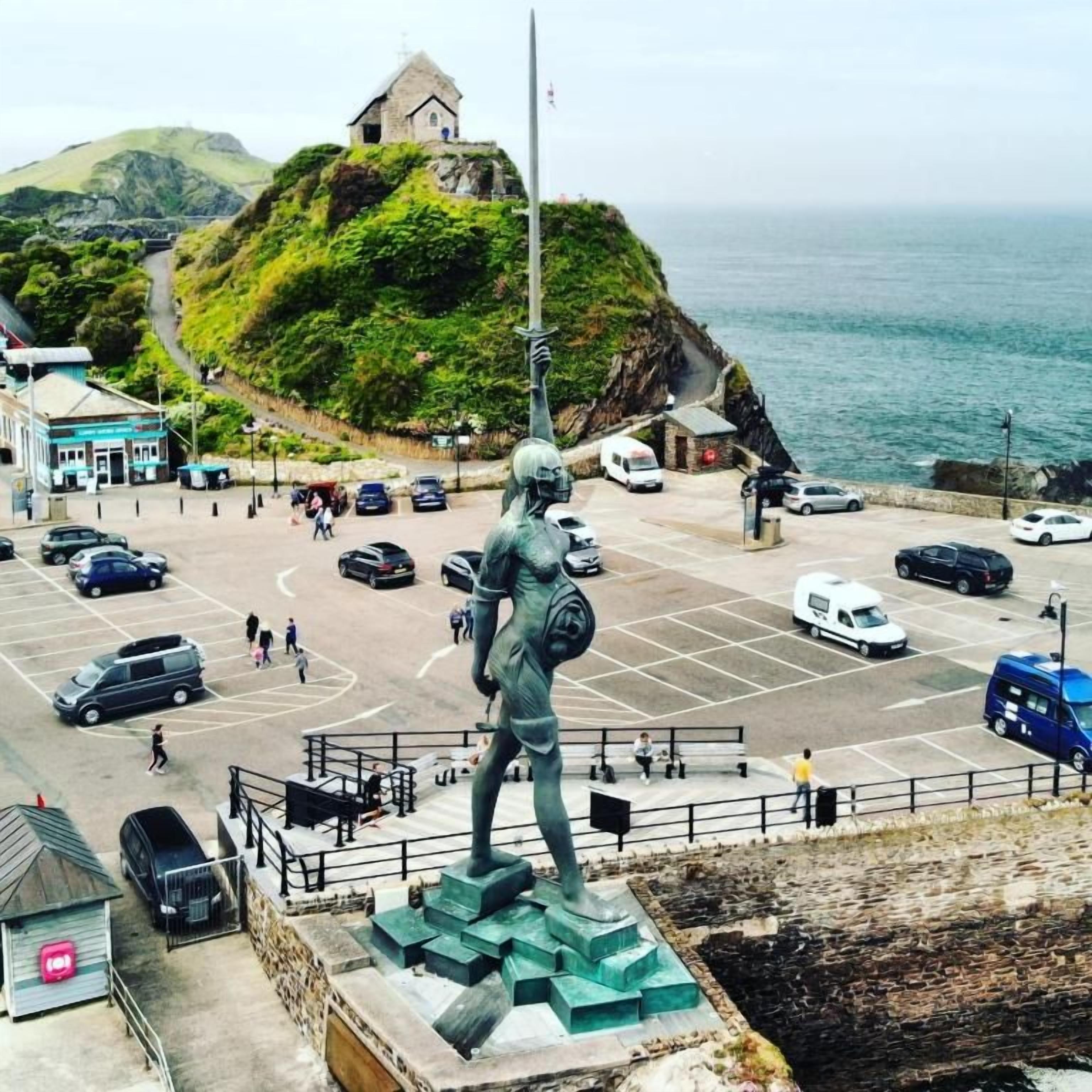 Una estatua en una plaza pública con un estacionamiento y edificios al fondo.