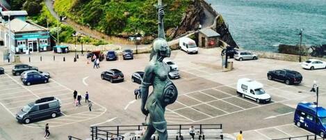 Una estatua en una plaza pública con un estacionamiento y edificios al fondo.